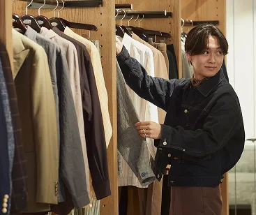 ハンガーにかかっている商品の袖を伸ばしているタカハラさん